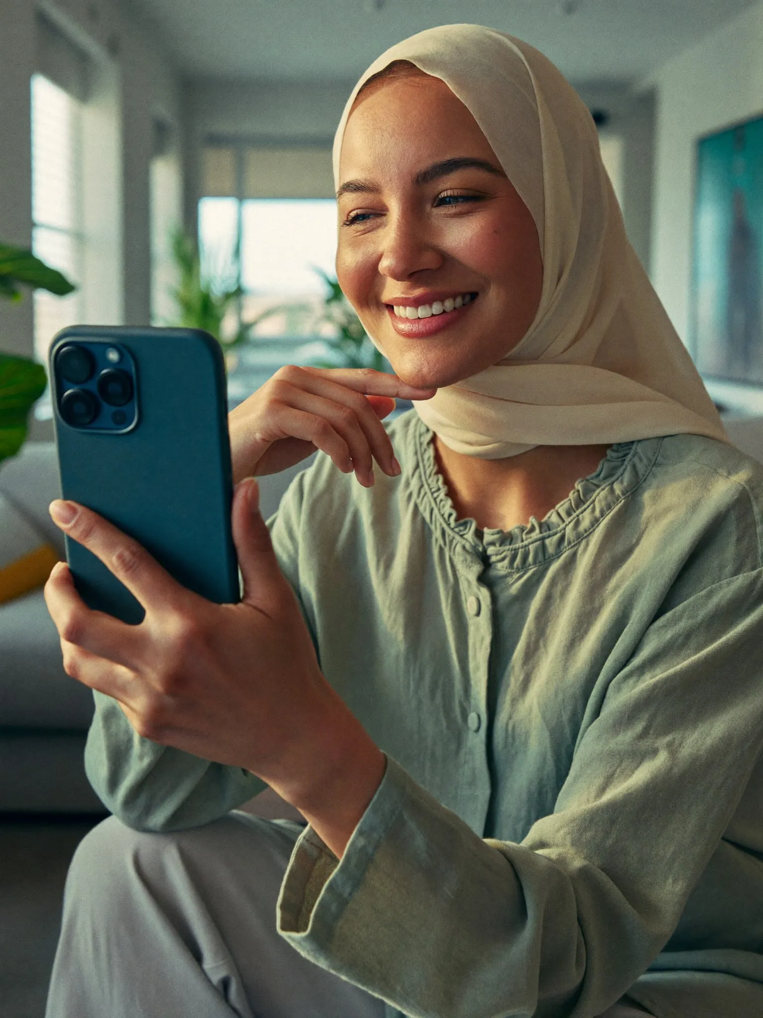 A woman wearing a hijab smiling at her phone during a video visit
