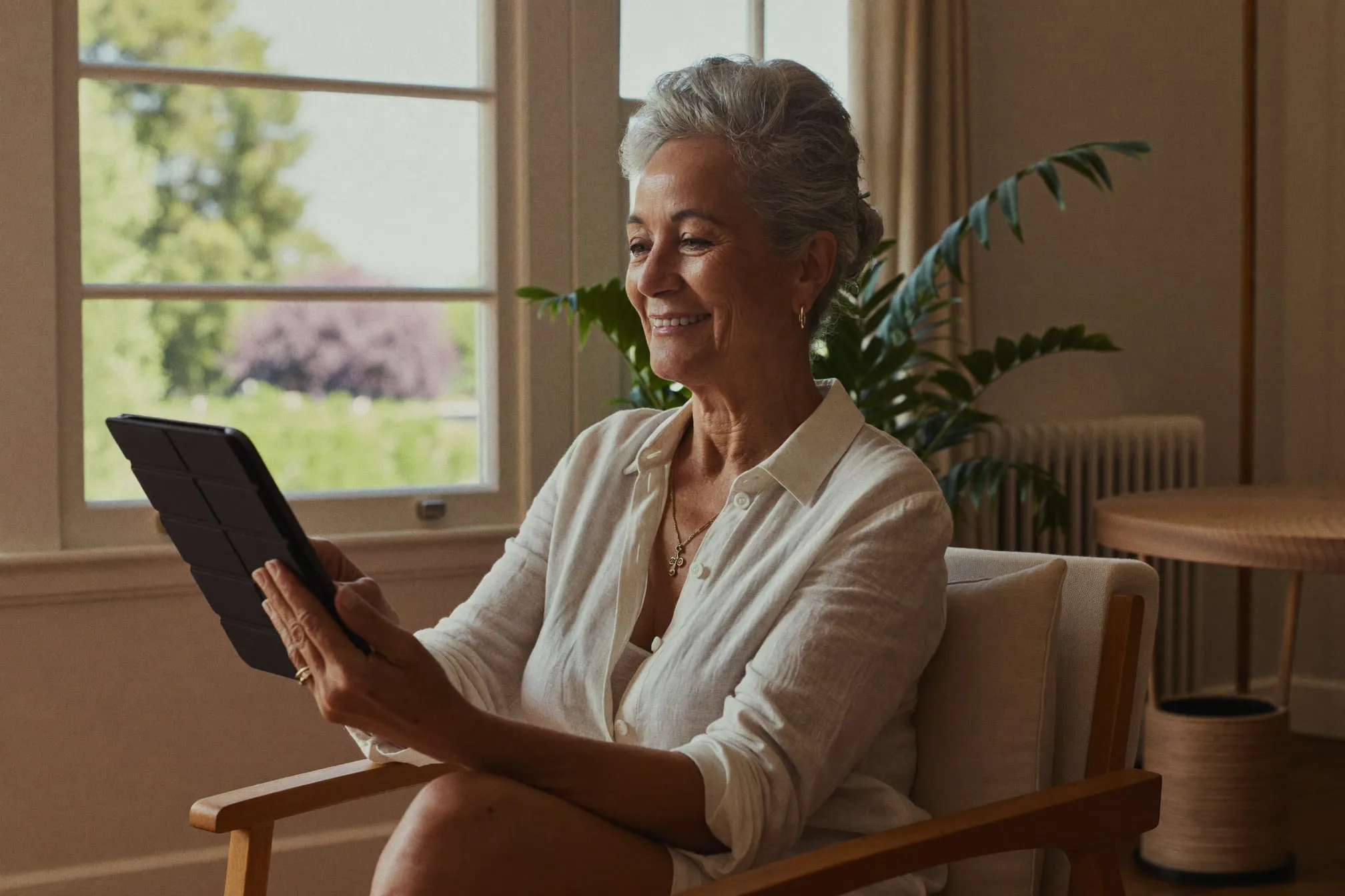 A woman by a window smiling at her tablet during a video visit